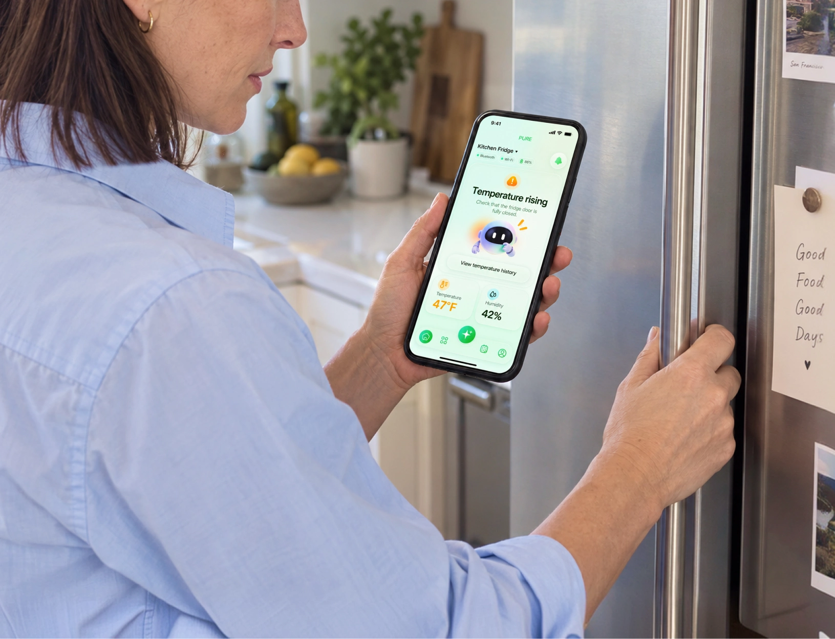A woman checking a rising fridge temperature alert in the PURE app beside her refrigerator